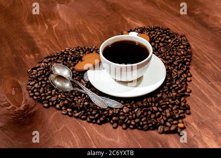 White coffee mug, heart shaped gingerbread and two spoons on a heart shaped base made from coffee beans - image Stock Photo