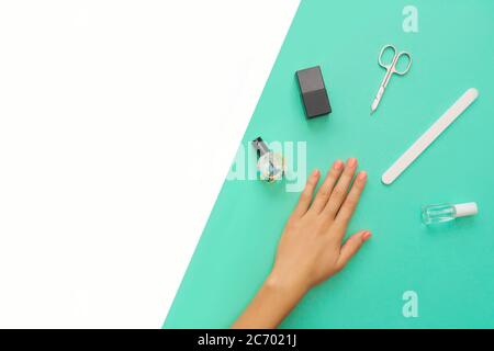 Beautifully manicured orange nails on the mint background with tools for manicure. Flat lay. Place for text. Stock Photo