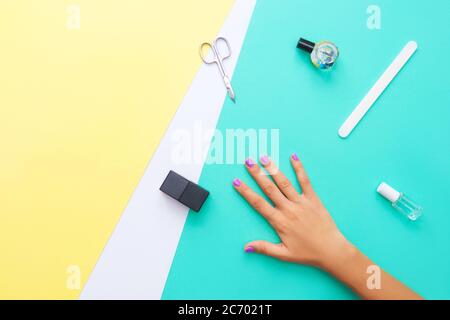 Beautifully manicured violet nails on the mint background with tools for manicure. Flat lay. Place for text on yellow background. Stock Photo