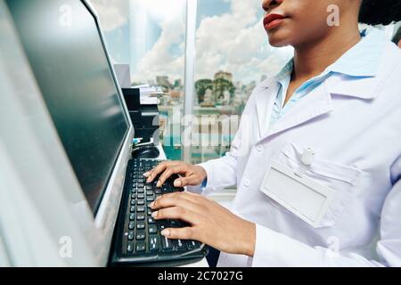 Cropped image of serious young Black female doctor working on computer in clinic and checking documents of patient Stock Photo