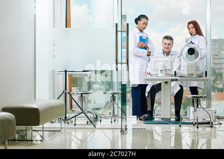 Group of ophthalmologists gathed at computer to discuss tests results of patient and make diagnosis Stock Photo
