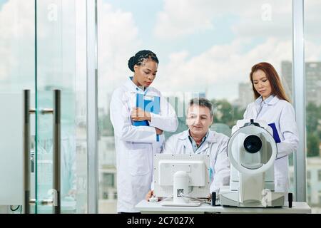 Smiling mature doctor showing results of medical test to young female interns and asking them to diagnose disease Stock Photo