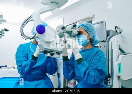 Asian female surgeon in scrubs using electronic microscope when operating patient Stock Photo