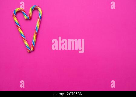 multicolored candy canes in the form of a heart on a pink background, copy space Stock Photo