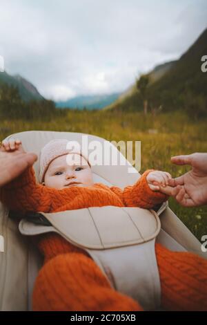 Baby sitting in bouncer family parents holding child hands mother and father travel childhood lifestyle outdoor summer vacations with kids Stock Photo