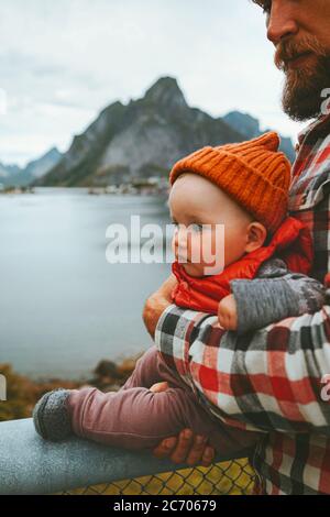 Child traveling with father in Norway family lifestyle outdoor summer vacations baby fashion kid wearing orange hat and red vest sightseeing Reine vil Stock Photo