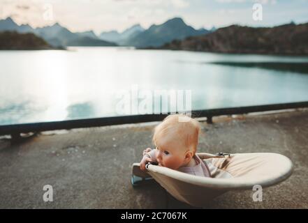 Child traveling in Norway family vacation lifestyle outdoor infant baby sitting in chair enjoying sunset mountains and fjord view Stock Photo