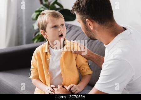 father touching shoulder of socked son while talking to him on sofa Stock Photo