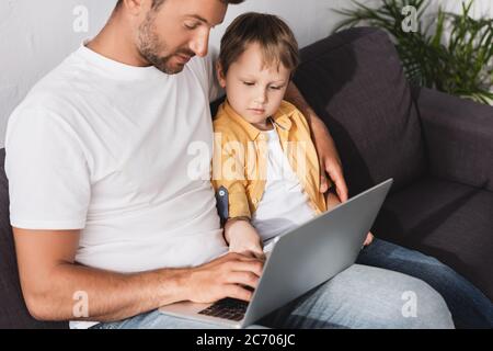 attentive father and son using laptop while sitting on sofa at home Stock Photo