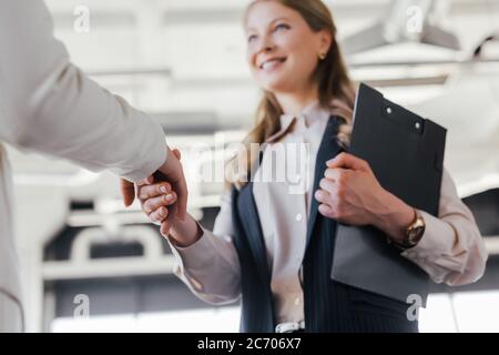 selective focus of smiling businesswoman shaking hands with coworker in office Stock Photo