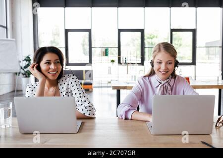 happy operators in headsets smiling while working in office Stock Photo