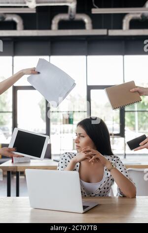 businesswoman sitting near coworkers holding gadgets with blank screen, notebook and papers Stock Photo