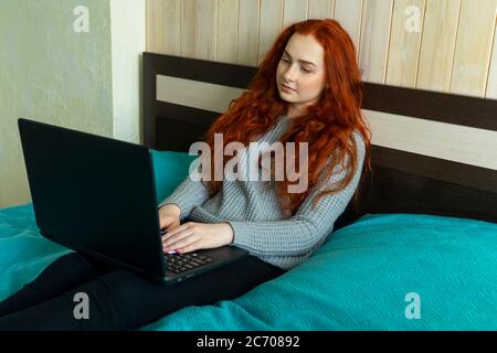Red-haired woman using laptop in bed home. Freelance. Stock Photo