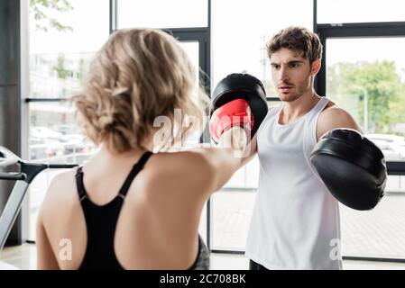 back view of sportive woman in boxing gloves exercising with man in boxing pads Stock Photo