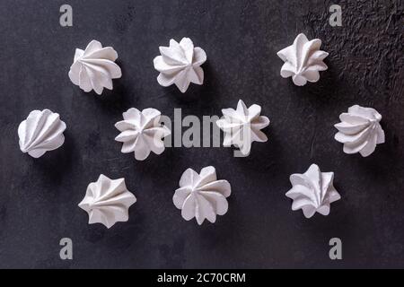 Pattern with ten white meringue cookies on black textured stone table surface. Sweet background, flat lay, directly above view. Unhealthy food concept Stock Photo