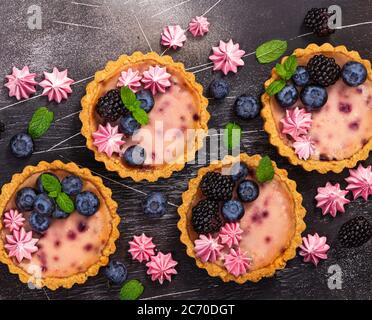 Four round shaped cheesecakes with fresh blackberries, blueberries, meringue and mint on a gray stone background. Stock Photo
