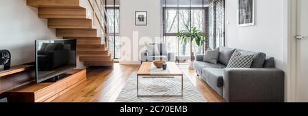 Panorama of two-floor apartment with spacious living room with wooden stairs and hardwood floor Stock Photo