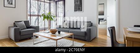 Stylish living room with corner windows with blinds and hardwood floor, panorama Stock Photo