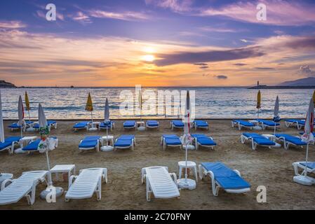 Looking out to the Aegean Sea beyond chairs and umbrellas lined up along the beach during sunset in Kusadasi, Turkey Stock Photo