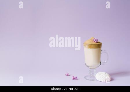 Beautiful dalgona drink a frothy coffee in a transparent mug and flowers lilac to purple Il purple background. Next to the mug is a marshmallow. Copy Stock Photo