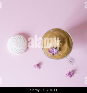 Beautiful dalgon coffee drink. Coffee mug with foam and lilac flower on a lilac pink background. Top view Stock Photo