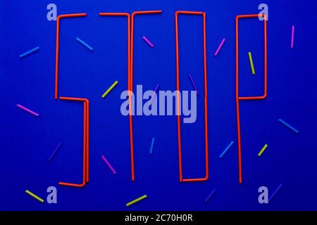 Word of stop from disposable tubes on blue background. Ocean pollution symbol. Multi-colored parts of tubes around word. Stock Photo