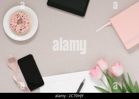 Trendy stylish frame for a female blogger, freelancer: pink diary, tablet, phone, Donat on a plate, pink tulips and an open Notepad with a clean page Stock Photo