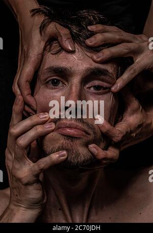 Four hands distort a mans face, he appears depressed and helpless Stock Photo