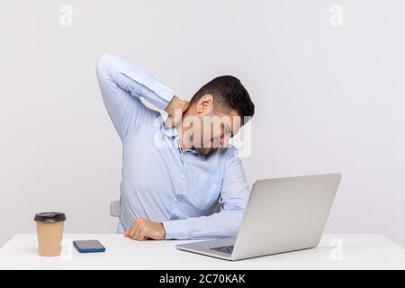 Tired male employee sitting office workplace, touching sore back neck, massaging hurting shoulders, painful stiff muscles, feeling exhausted fatigued. Stock Photo