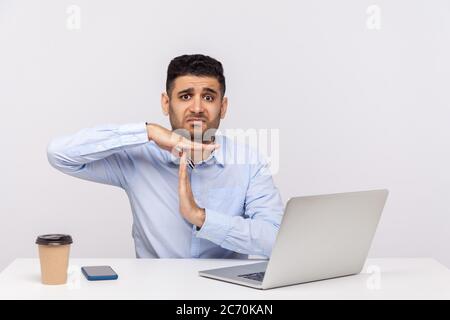 Need break! Upset man employee sitting office workplace with laptop on desk, looking imploring and showing time out gesture, worried about deadline. i Stock Photo