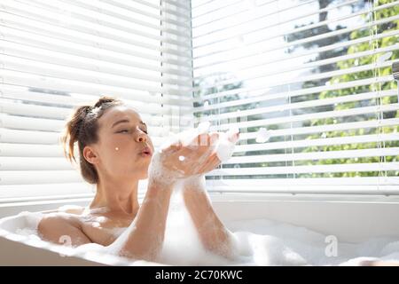 Woman blowing soap bubbles in a bathtub Stock Photo