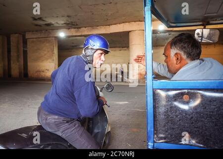 New Delhi / India - February 18, 2020: man riding motorbike with helmet and white moustache asking for directions to tuk tuk driver in India Stock Photo