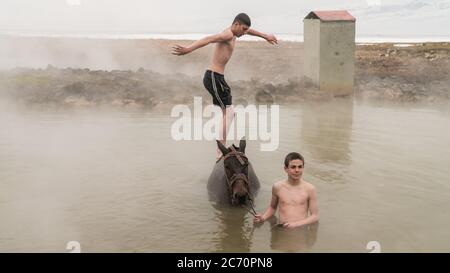 Guroymak, Bitlis, Turkey - February 2020: Young boy jumping into thermal water from his horse, animal shower Stock Photo