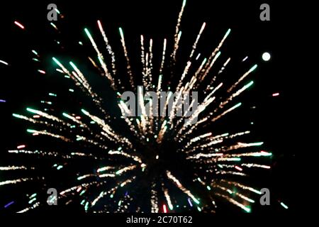 a close up single explosion of a spider rocket firework with a full moon to the side from a new york city rooftop against a night sky Stock Photo