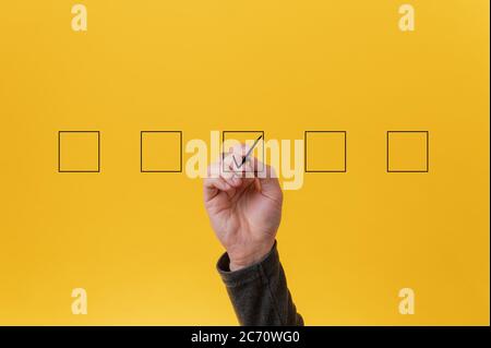 Male hand drawing a check mark in the middle box in a row of five. Over yellow background. Stock Photo