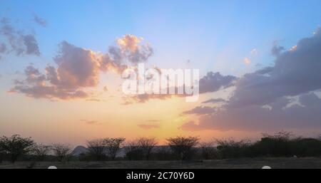 An orange sunset against a blue sky in the shade of trees Stock Photo