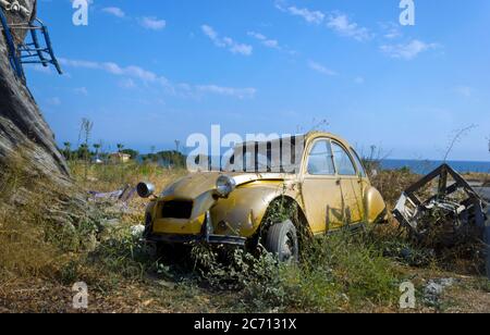 Abandoned gold coloured Citroen 2cv car wreck, Northern Cyprus with blue sky on waste ground copy space with ocean in background Stock Photo