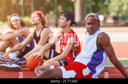 Black basketball player with his diverse team resting at outdoor court after challenging game, free space Stock Photo