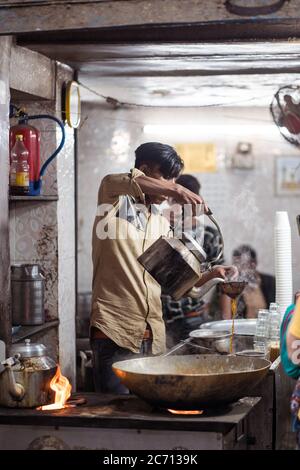 New Delhi / India - February 18, 2020: young indian man working preparing milk tea in traditional teahouse in Old Delhi Stock Photo