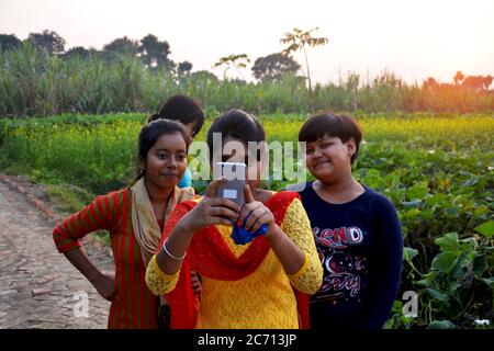An Indian teenage girl taking pictures through mobil phone and friends looking, selective focusing Stock Photo