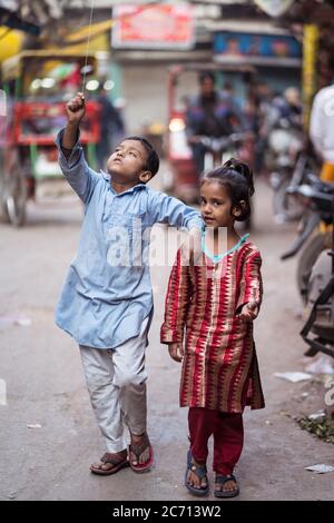 New Delhi / India - February 18, 2020: little girl and boy siblings carrying balloon walking in street of Old Delhi Stock Photo