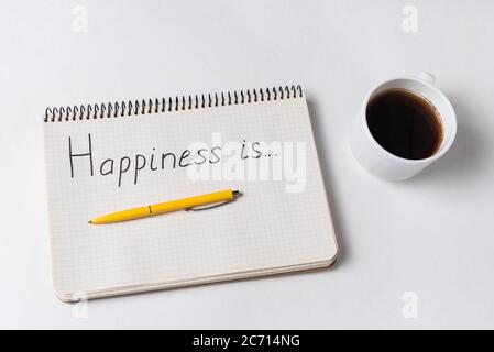 HAPPINESS IS, inscription in the notebook on white background. Top view of notebook, coffee and pen Stock Photo