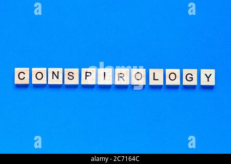 Conspirology - words made of wooden blocks with letters, secret plan of powerful people, conspiracy theory concept, top view blue background. Stock Photo