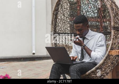 Business african american man holding smartphone, dictating voice message, recording audio, using voice mic. People works outdoors Stock Photo