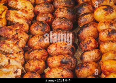 Closeup of freshly baked potato with spices and chicken wings on skewers. Charcoal baked vegetables. Street food in the market. Grilled potatoes to go Stock Photo