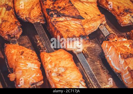 Closeup of juicy fatty fried pieces of red fish on metal skewers with shallow depth of field in a street market. Street food in the tourist area of  Stock Photo