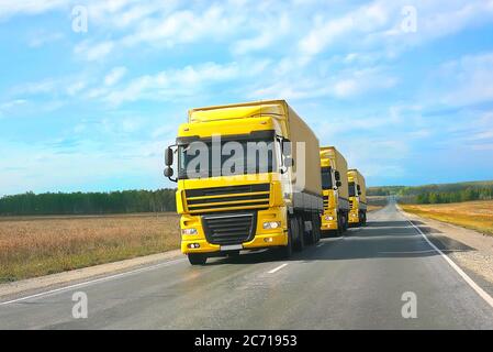 escort of yellow trucks on country road Stock Photo