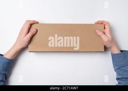 Child holds rectangular craft paper box on white background. Parcel delivery concept. Top view. Copy space Stock Photo