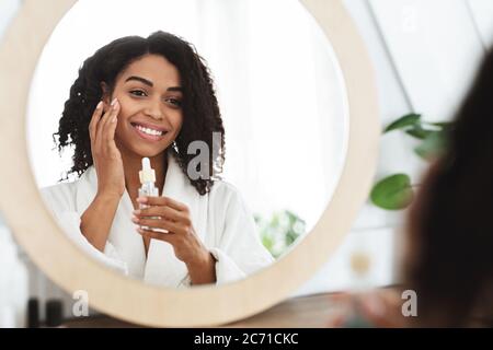 Skin Hydration. Positive black woman applying moisturizing serum on face Stock Photo