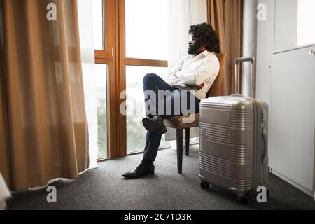 Black man businessman sitting and looking at window in hotel room Stock Photo